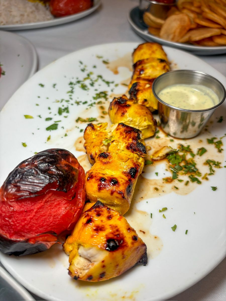 Saffron Chicken Kabob with a grilled tomato and a cup of sauce