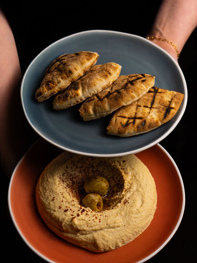 A plate of grilled pita held above a plate of hummus