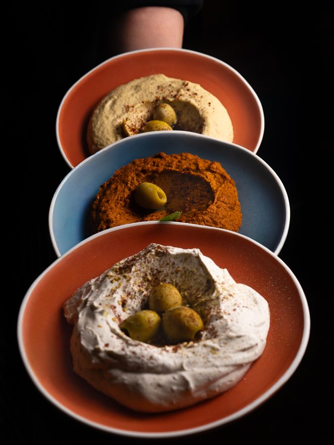 Three dips carried to the table: hummus, muhammara and labneh with olives