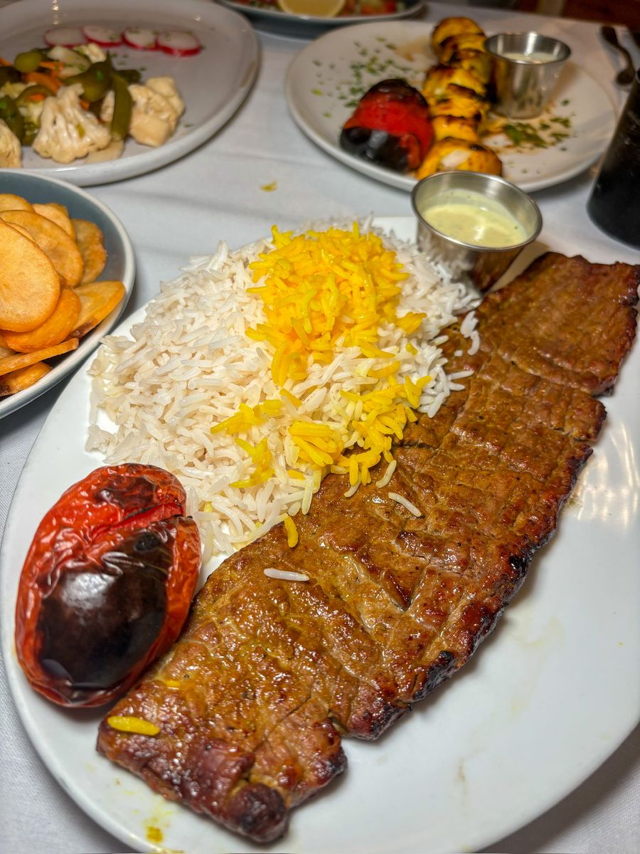 A kabob plate with saffron rice and a grilled tomato