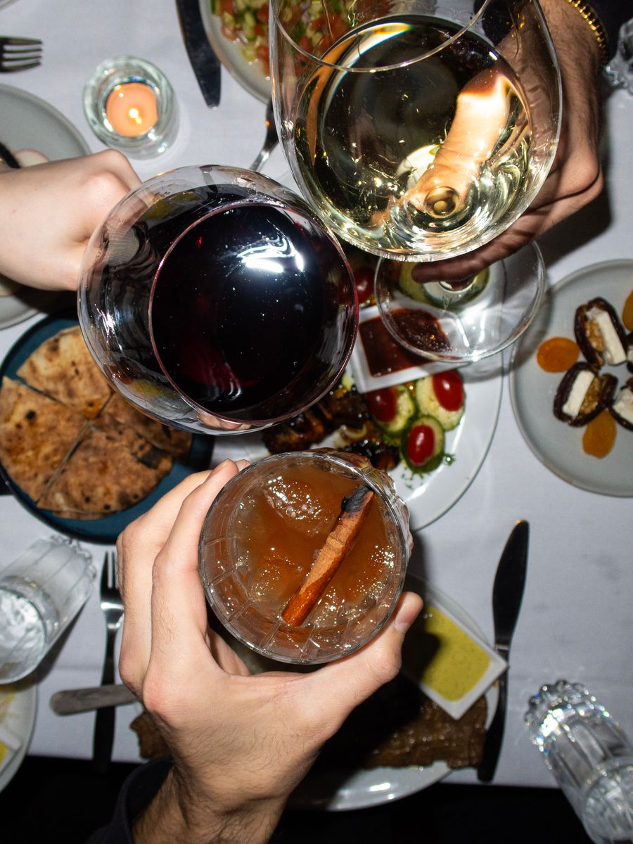 Glasses of red and white wine meeting over a table of shared plates, seen from above