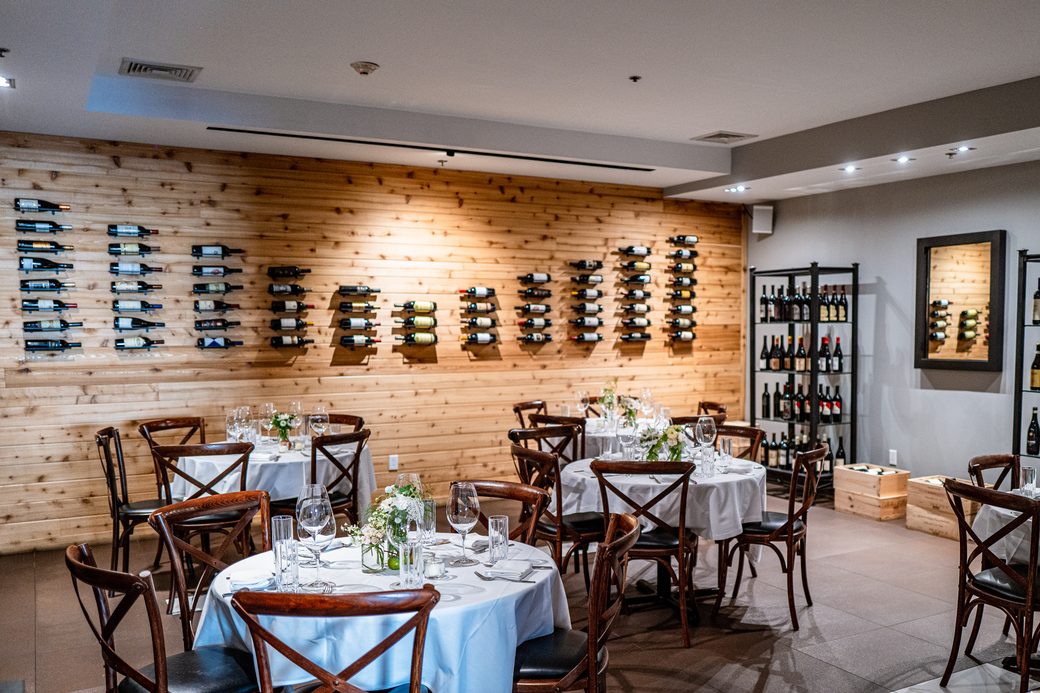 The private dining room in White Plains, round tables set before a cedar wall of wine