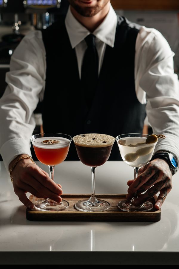 A bartender presenting three cocktails on a wooden tray