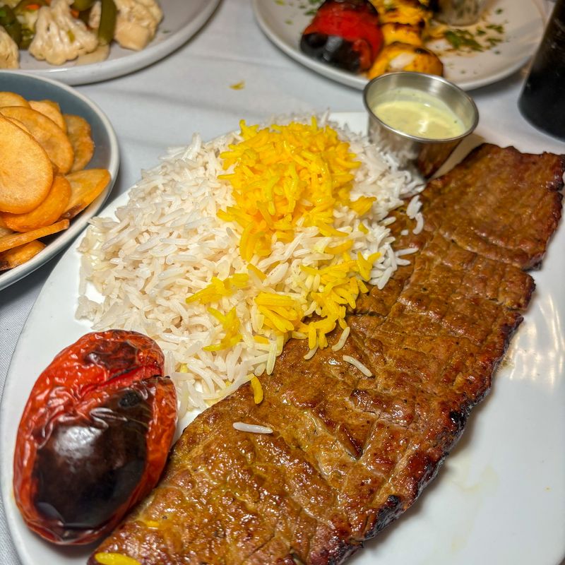 A kabob plate with saffron rice and a grilled tomato